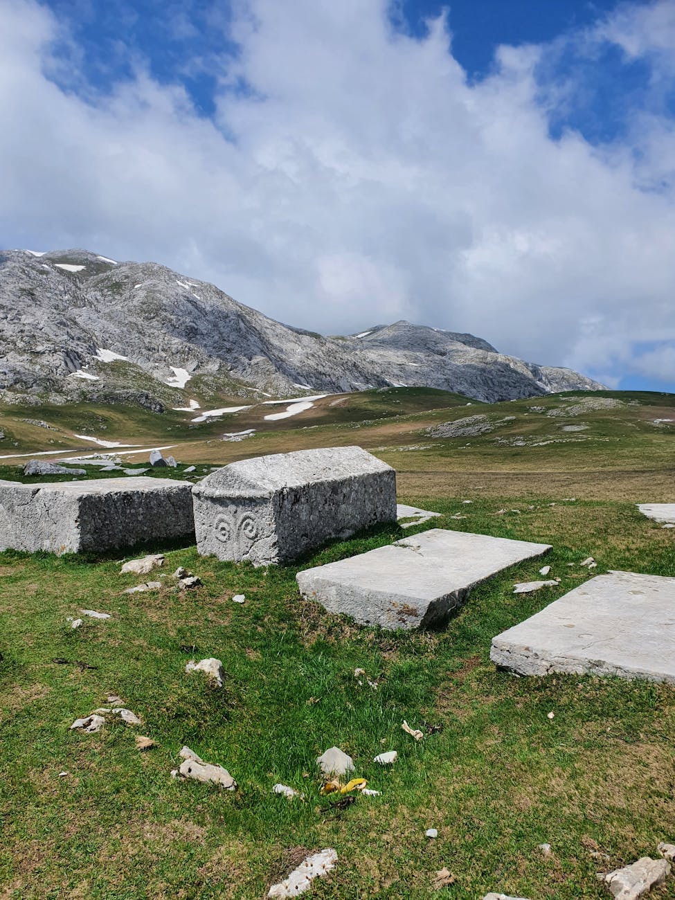 gray concrete blocks on green grass field near gray mountain under white clouds